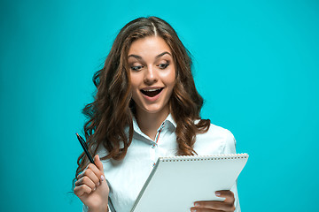 Image showing Surprised young business woman with pen and tablet for notes on blue background