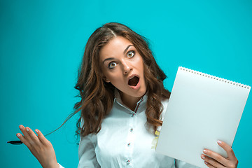 Image showing Surprised young business woman with pen and tablet for notes on blue background