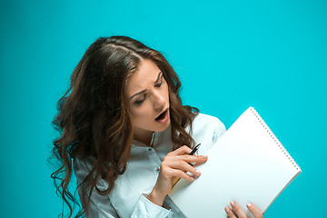 Image showing Surprised young business woman with pen and tablet for notes on blue background