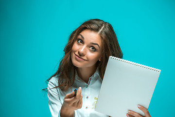 Image showing Surprised young business woman with pen and tablet for notes on blue background