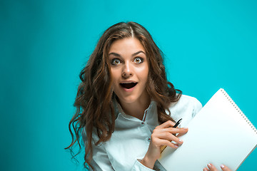 Image showing Surprised young business woman with pen and tablet for notes on blue background