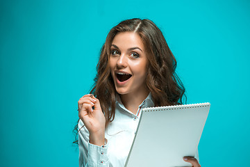 Image showing Surprised young business woman with pen and tablet for notes on blue background