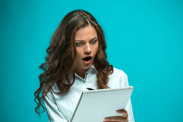 Image showing Surprised young business woman with pen and tablet for notes on blue background