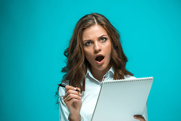 Image showing Surprised young business woman with pen and tablet for notes on blue background