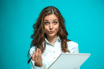 Image showing Surprised young business woman with pen and tablet for notes on blue background