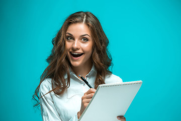 Image showing Surprised young business woman with pen and tablet for notes on blue background