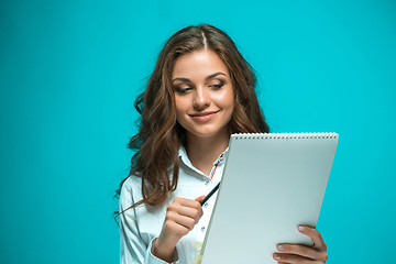 Image showing The smiling young business woman with pen and tablet for notes on blue background