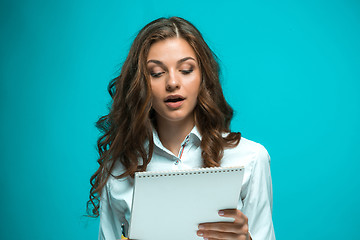 Image showing Surprised young business woman with pen and tablet for notes on blue background