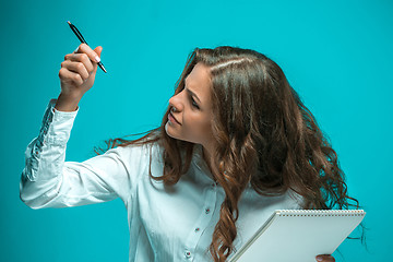 Image showing The displeased young business woman with pen and tablet for notes on blue background