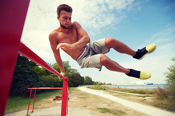 Image showing young man exercising on horizontal bar outdoors