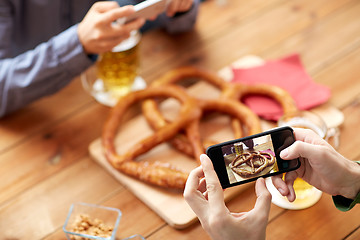 Image showing close up of hands picturing pretzel by smartphone