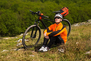 Image showing Young man sitting near the cycle on a green meadow