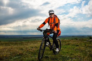 Image showing Young man cycling on a rural road through green meadow