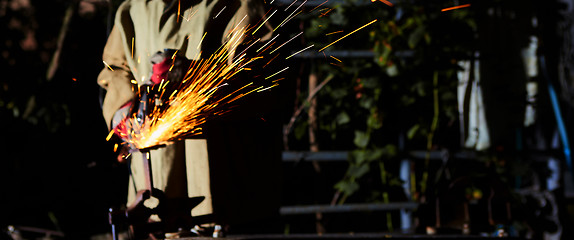 Image showing Worker cutting metal with grinder. Sparks while grinding iron