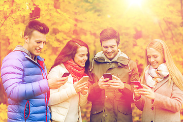 Image showing smiling friends with smartphones in city park