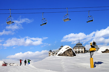 Image showing Chair-lift in blue sky and three skiers on ski slope at sun nice