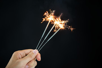 Image showing hand holding sparklers over black background