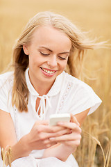 Image showing happy young woman with smartphone on cereal field