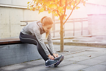 Image showing happy young sporty woman tying shoelaces outdoors