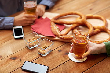 Image showing close up of hands with smartphones and beer at bar