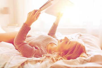 Image showing young woman reading book in bed at home