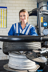 Image showing Confident Female Mechanic Mounting Car Tire On Rim In Garage