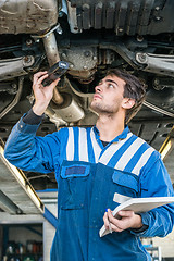 Image showing Mechanic Holding Flashlight While Examining Car Exhaust System
