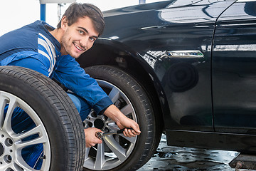 Image showing Confident Mechanic Changing Car Tire At Automobile Shop