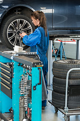 Image showing Female Mechanic Changing Tire From Suspended Car In Garage