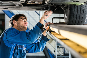 Image showing Mechanic Changing Tire From Suspended Car At Automobile Shop