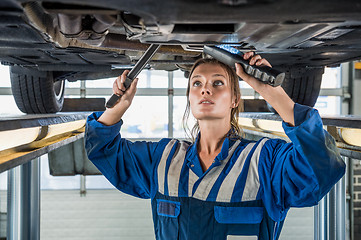 Image showing Female Mechanic Using Flashlight While Repairing Car On Lift
