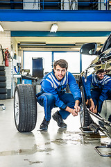 Image showing Mechanic Crouching While Changing Car Tire At Garage