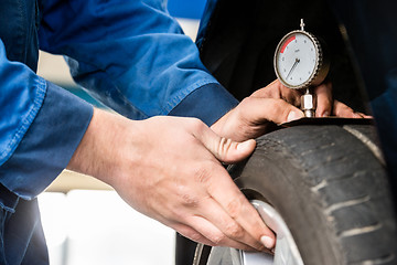 Image showing Hands Of Mechanic Pressing Gauge Into Tire In Garage