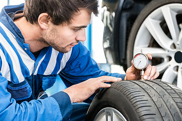 Image showing Young Male Mechanic Pressing Gauge Into Tire In Garage