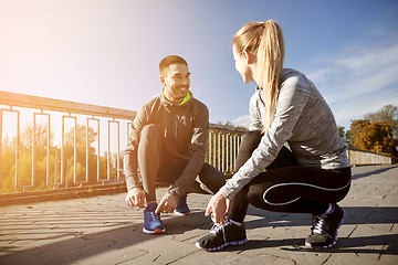 Image showing smiling couple tying shoelaces outdoors