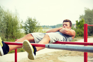 Image showing young man doing sit up on parallel bars outdoors