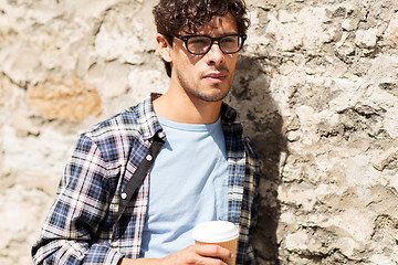 Image showing man in eyeglasses drinking coffee over street wall