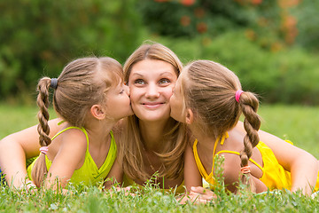 Image showing Two daughters kissing mother lying on the grass on a picnic, Mother looked up fun