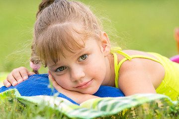 Image showing Five-year girl lies on a bed on a green meadow and touching looking to the frame