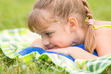 Image showing Five-year girl lies on a green meadow and touching looking at grass