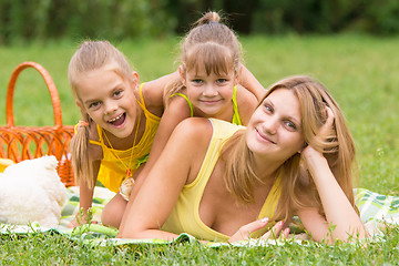 Image showing Mother and two daughters lie on each other on the green grass