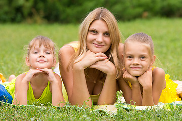 Image showing Mother and two daughters lie on the green grass and propping up hands a head looked in the picture