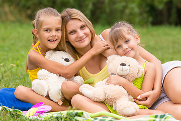 Image showing Two daughter kissing and hugging her mother lying on the grass on a picnic