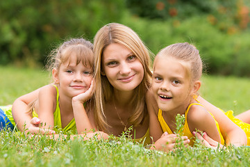 Image showing Mother and two daughters lie on the green grass, and looked into the frame