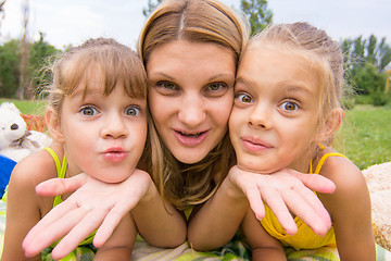 Image showing Two girls resting her head on her mother\'s palm and fun look into the frame