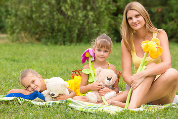 Image showing Mother and daughter sitting with soft toys on a picnic and watch the shot