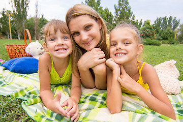 Image showing Mother and two girls lying on the grass on a picnic and fun look into the frame