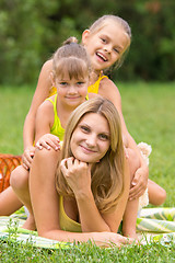 Image showing Two daughters are sitting on the young mother, who is lying on the green grass