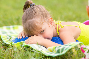 Image showing Five-year girl lies on a bed on a green meadow and artfully looks aside