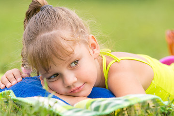 Image showing Five-year girl lies on a bed on a green meadow and thoughtfully looks aside